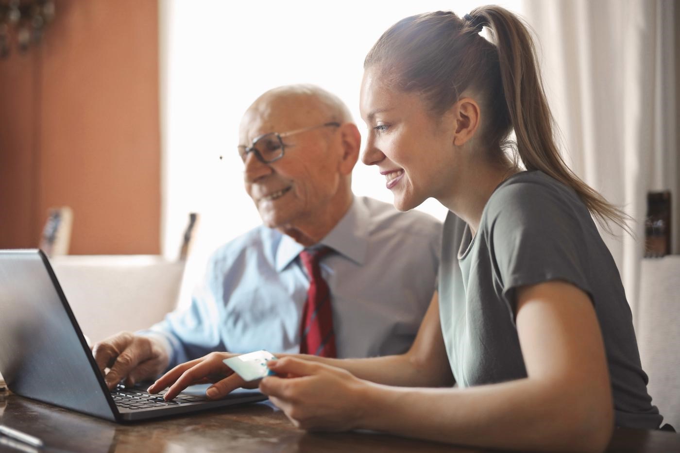 Young woman helping granddad with online banking on a laptop