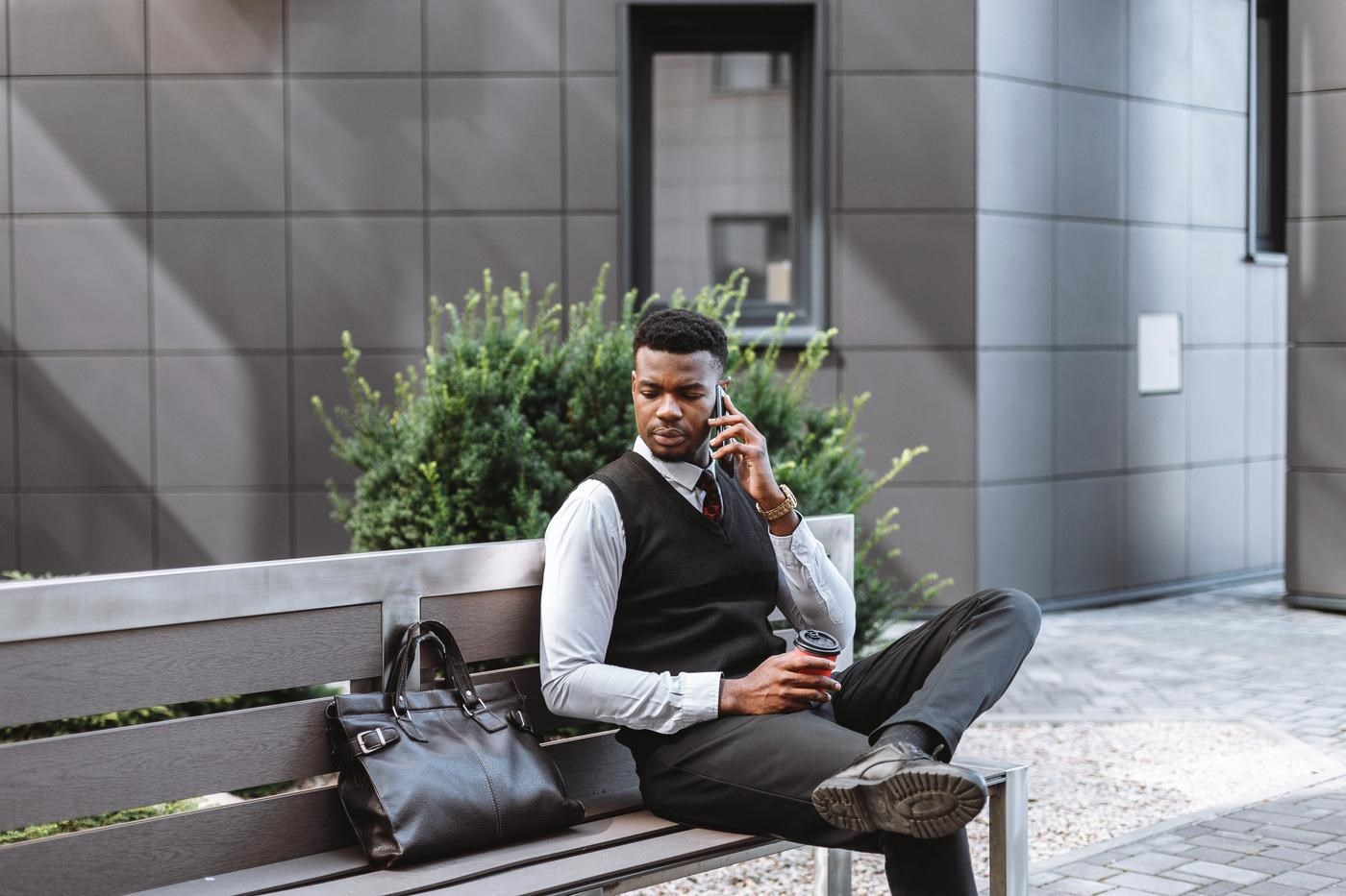 Young businessman sitting on a bench outside, talking on a phone