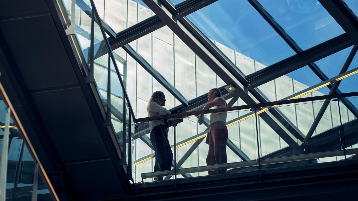 Two ladies talk standing in the skywalk in Tietoevry office